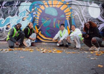 A brightly coloured mural with artists crouched beside it.